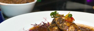 Jerk chicken with a bowl of rice and peas behind