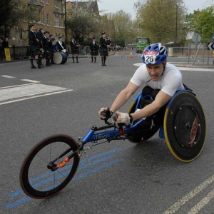 A wheelchair athlete passes through Rotherhithe with musical accompaniment from the pipe band by McTumshie