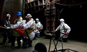 The group pauses inside a chamber, thigh-deep in effluent.
